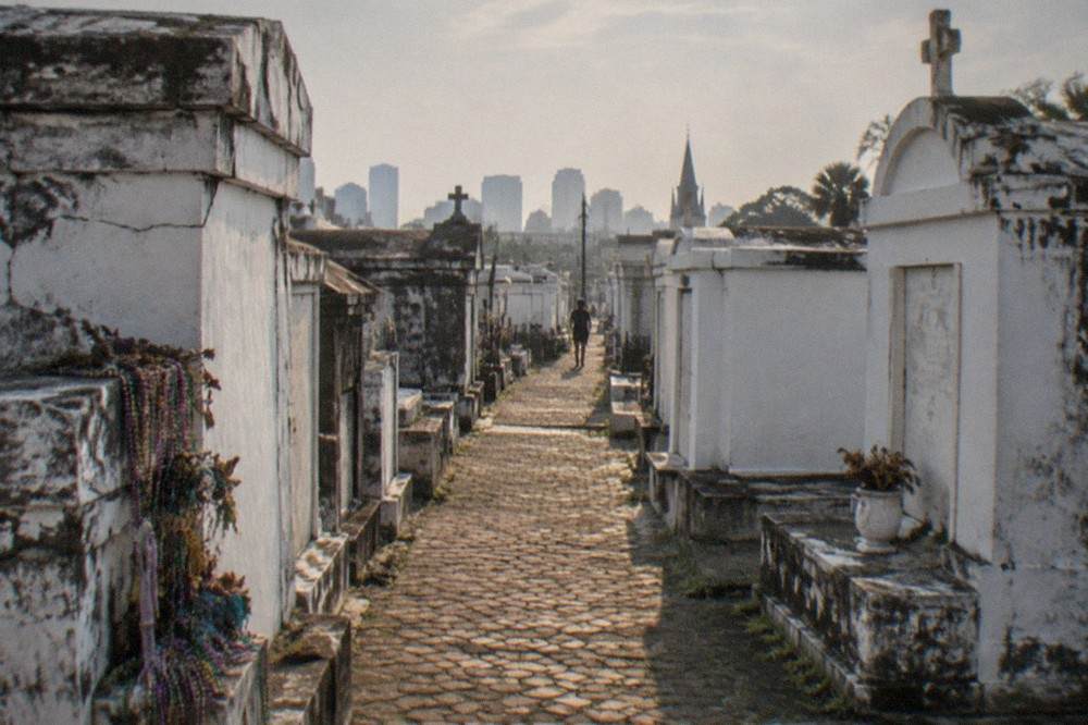A narrow brick path between faded white above-ground tombs in an old New Orleans cemetery