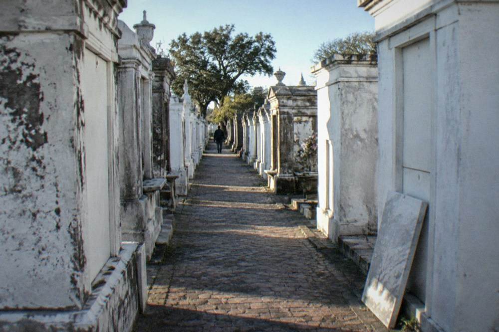 A narrow brick path between rows of tall white above-ground vaults in a New Orleans cemetery