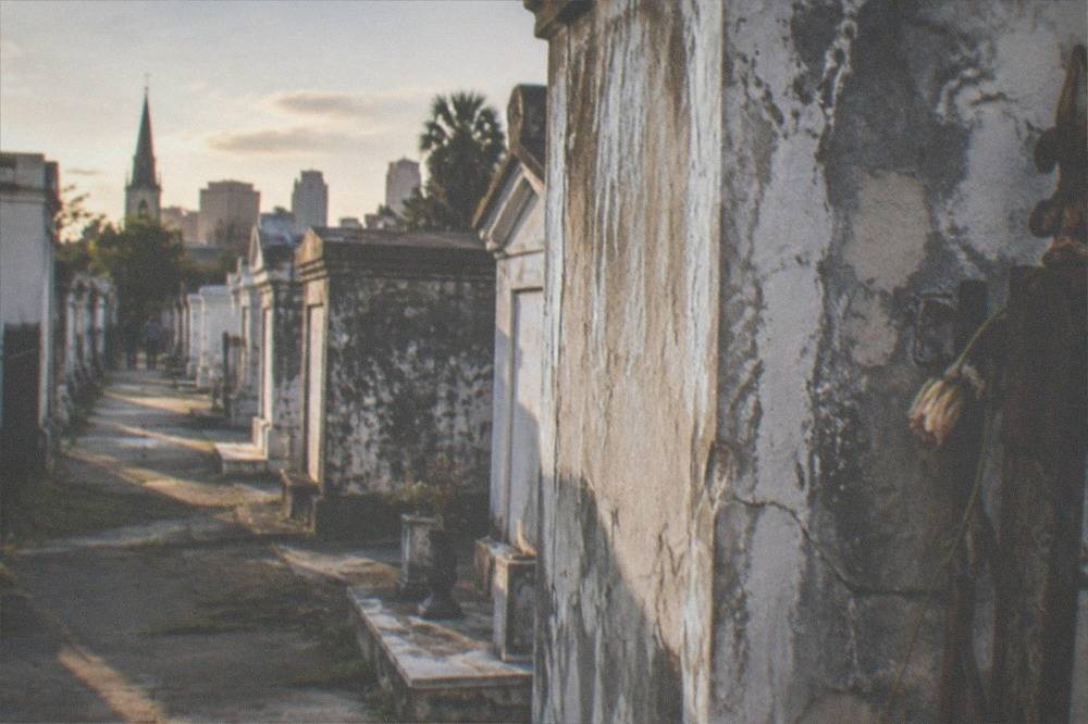 Sunlight falling across rows of faded plaster tombs in a quiet New Orleans cemetery