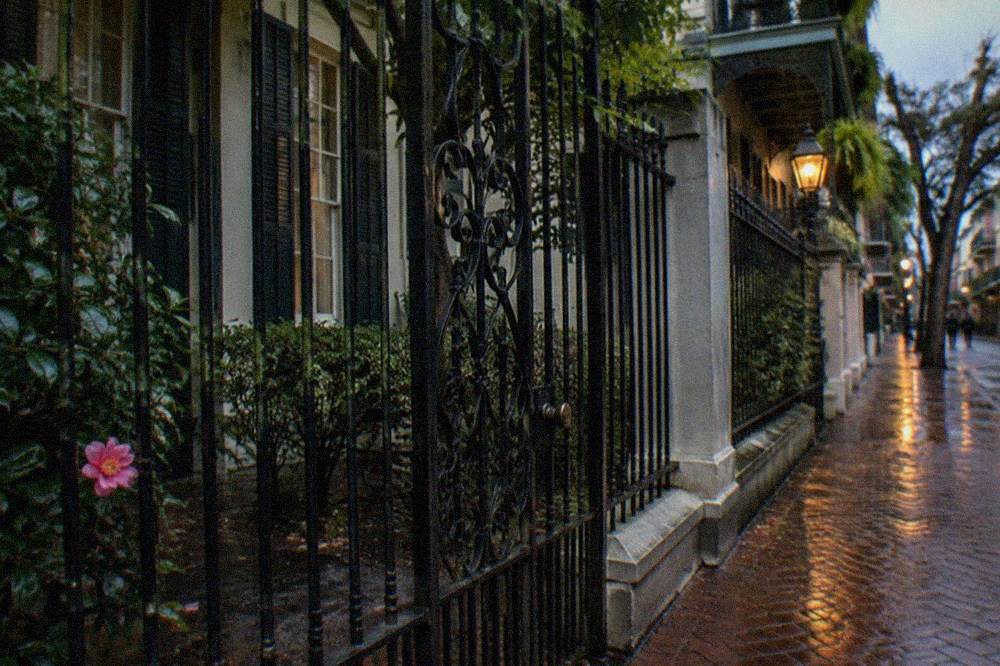 A closed wrought-iron gate and dark windows of a French Quarter mansion on a quiet evening street