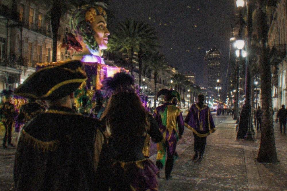 A night parade on a New Orleans street with costumed marchers and floats under streetlights