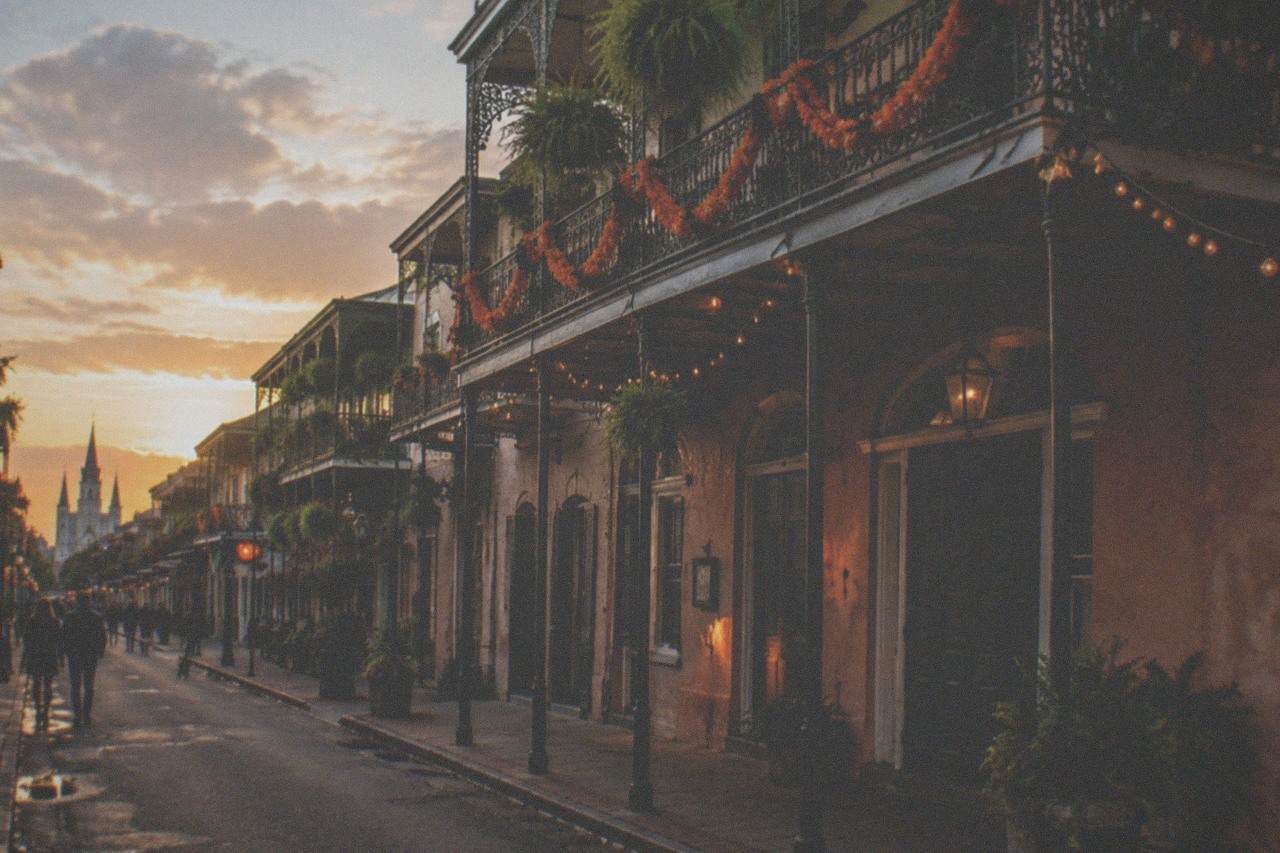 A French Quarter street at dusk with iron-laced balconies strung with Halloween decorations