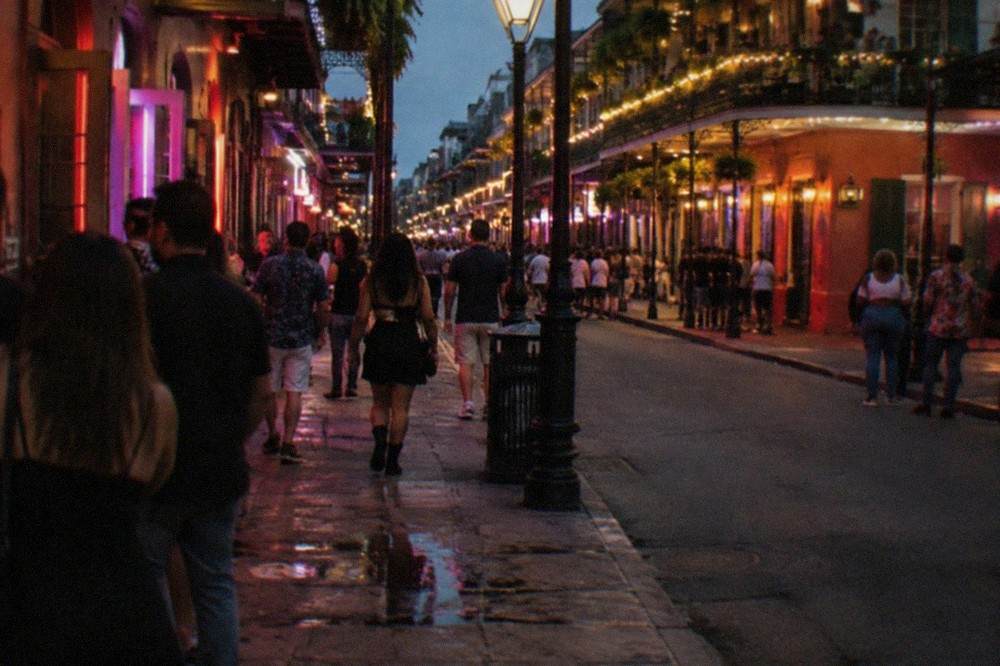 Crowded Bourbon Street sidewalk at night with neon bar signs and string-lit balconies above