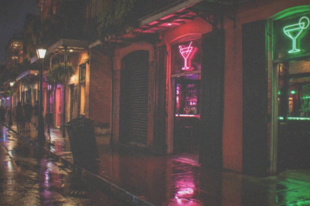 Neon cocktail and daiquiri shop signs glowing above a French Quarter sidewalk at night