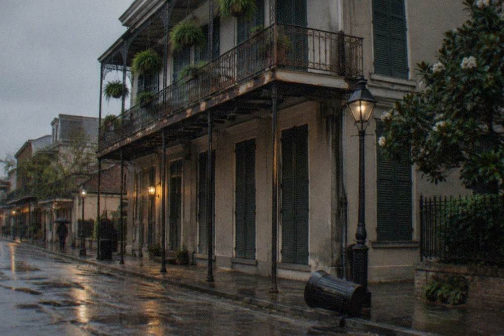 A dark three-story French Quarter townhouse facade with tall shutters and ironwork balconies seen from the street at dusk