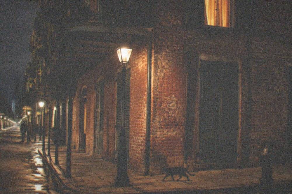 A lamplit French Quarter street corner with old brick buildings and closed shutters at night