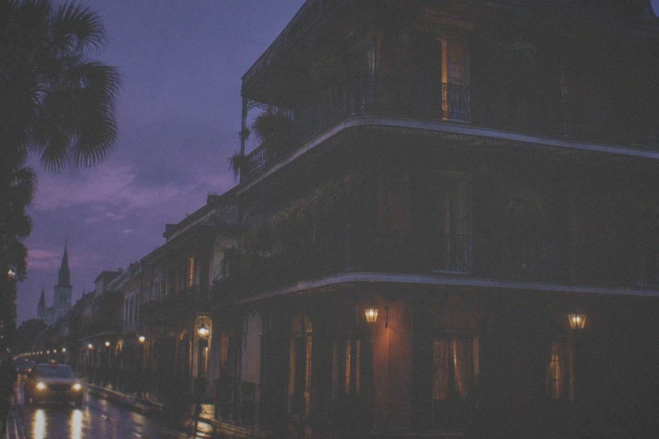 A tall French Quarter townhouse with ironwork balconies standing dark against an evening sky