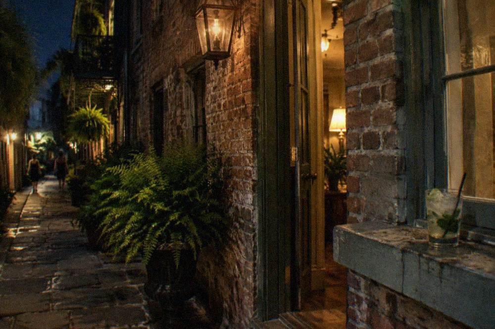 A narrow French Quarter alley at night with warm light spilling from a doorway onto old brick walls