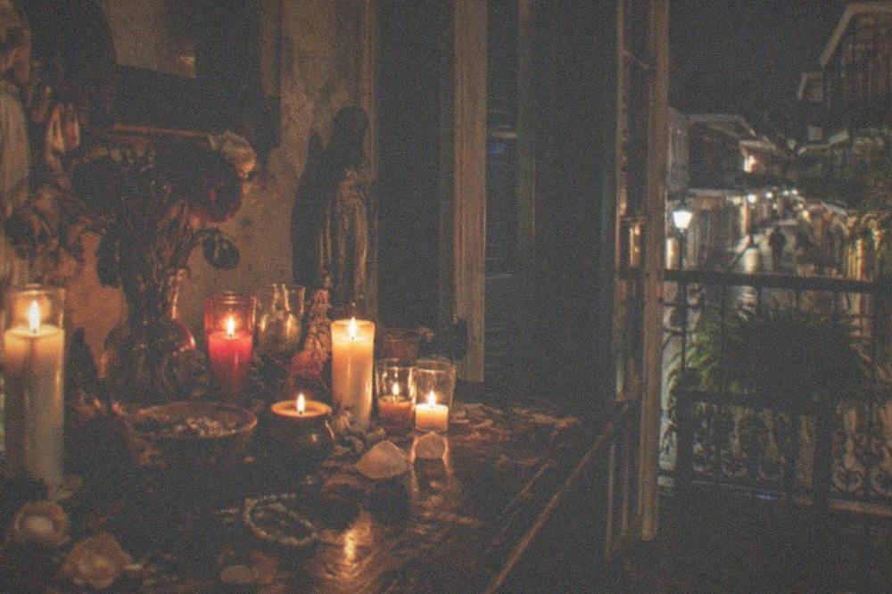 A candlelit altar with statues, flowers and offerings arranged on a dim wooden table