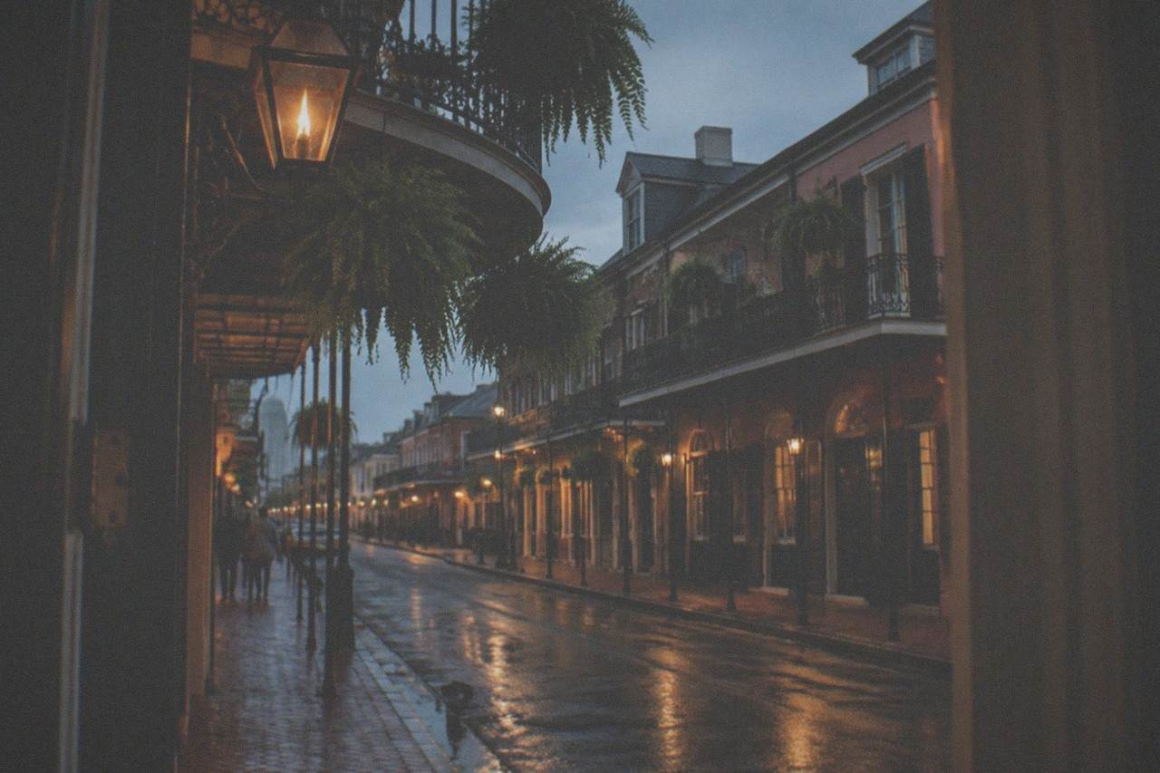 Ironwork balcony over a dim French Quarter street at dusk with gas-style lanterns
