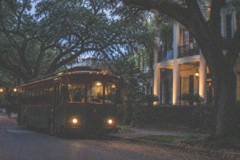 A tour bus parked near a Garden District mansion after dark, guests stepping off