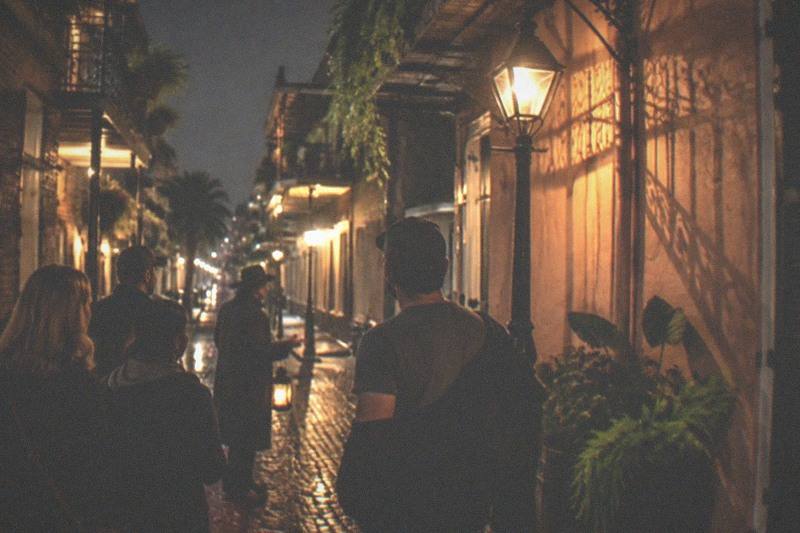 A guided ghost walk group stopped on a narrow French Quarter street at night, lantern raised