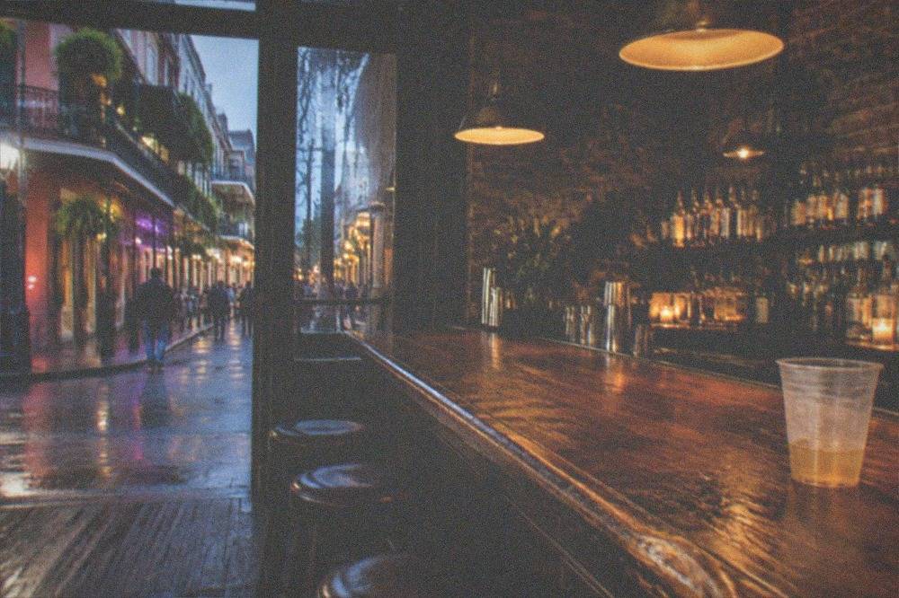 Dimly lit historic bar interior with wooden counter, hanging lamps and empty stools