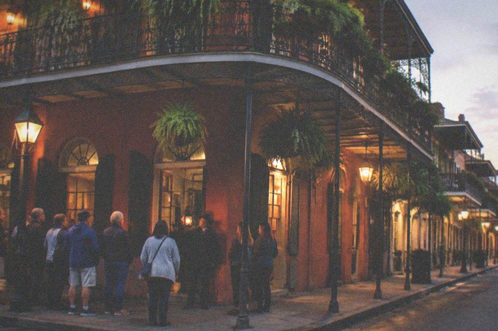 Evening crowd gathered under street lamps on a French Quarter corner with a lit guide lantern