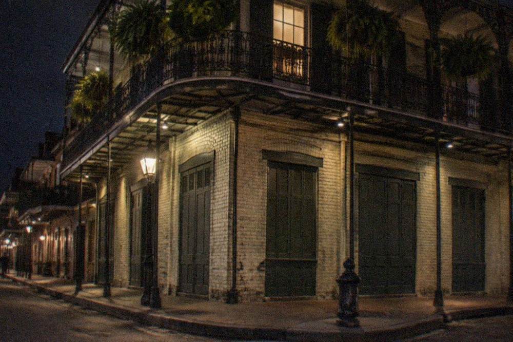 Night view of a lit French Quarter corner building with ironwork balconies above a closed storefront
