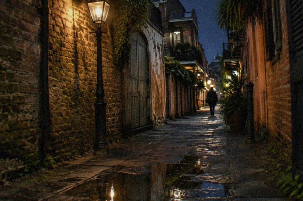 Gaslight-style street lamp glowing above a narrow French Quarter alley at night