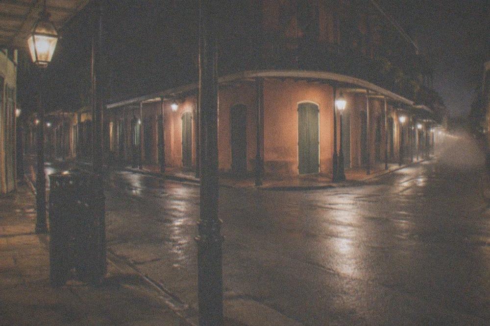 Empty lit intersection in the French Quarter at night with glowing street lamps and shuttered storefronts
