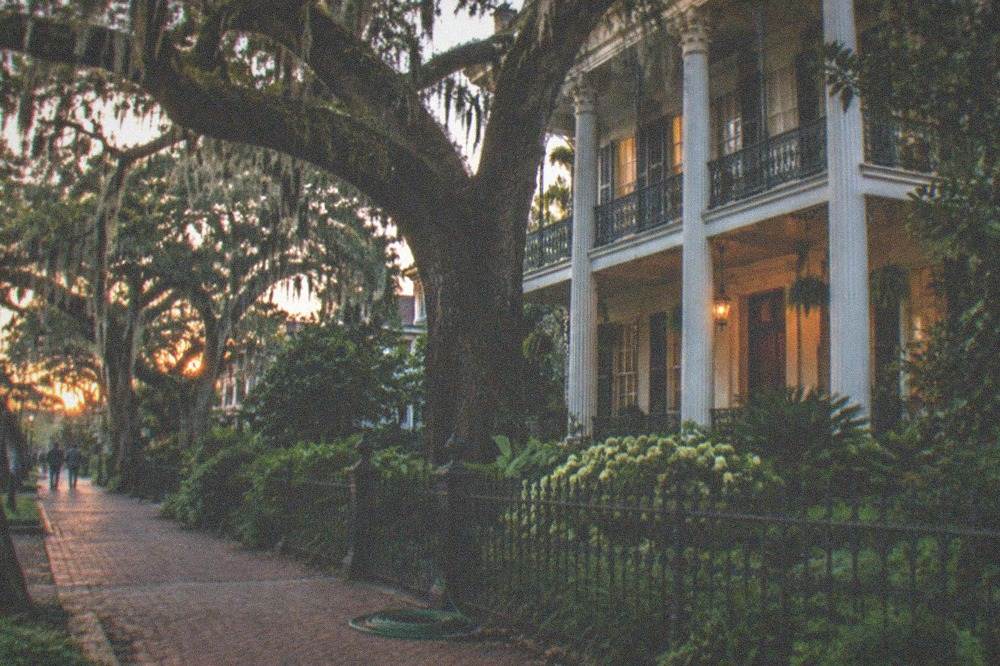 Historic Garden District mansion with columned porch and cast iron gallery behind live oaks