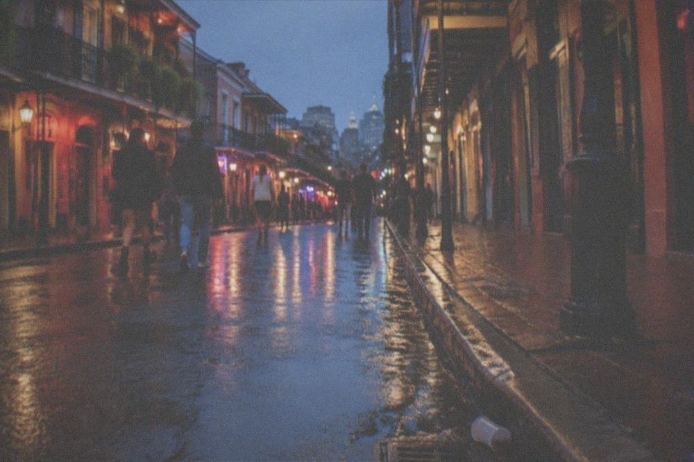 Nighttime French Quarter street with lit storefronts and pedestrians walking