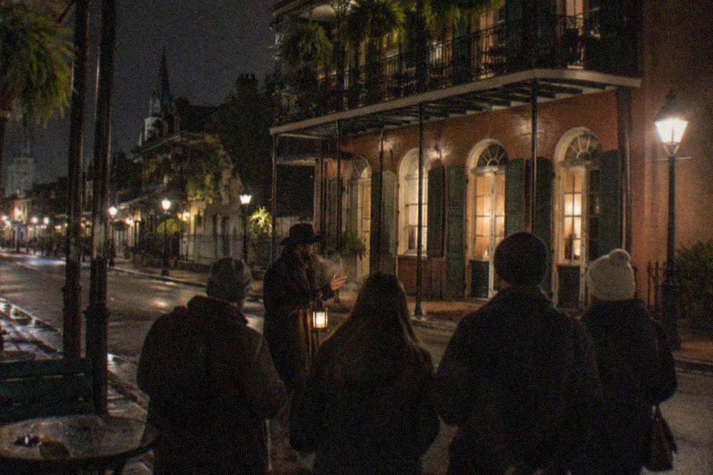 A tour guide holding a lantern addressing a small group on a dim French Quarter sidewalk