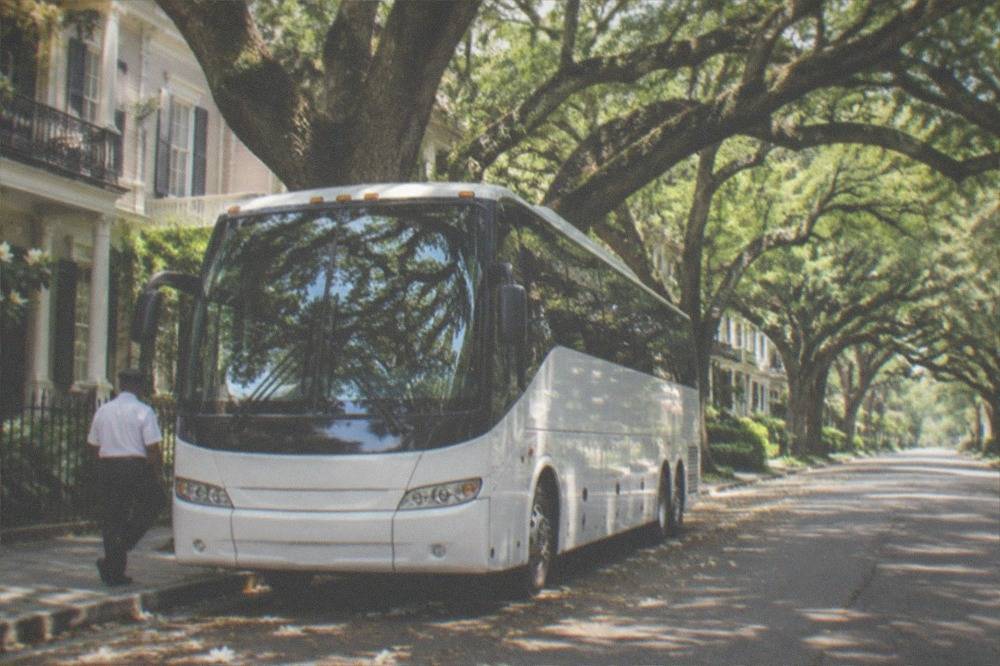 Tour bus parked on a New Orleans street lined with oak trees and historic buildings