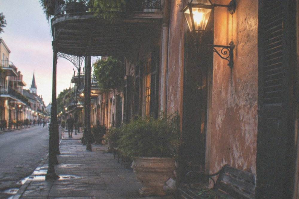 Lantern-lit French Quarter street corner at dusk with ironwork balconies