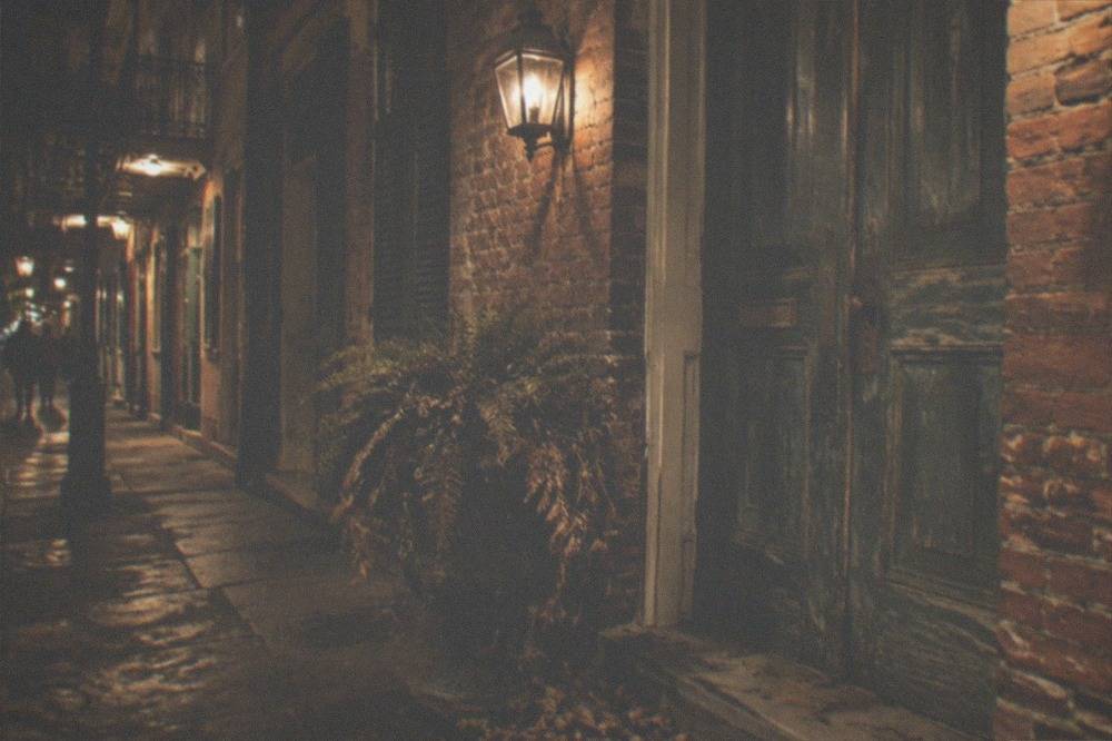 A quiet Royal Street doorway at night with lantern light on old brick