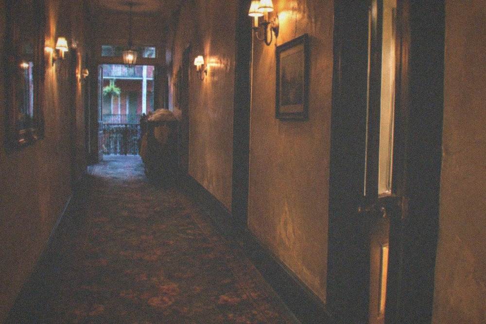 A dimly lit hotel corridor with antique carpet and wall sconces