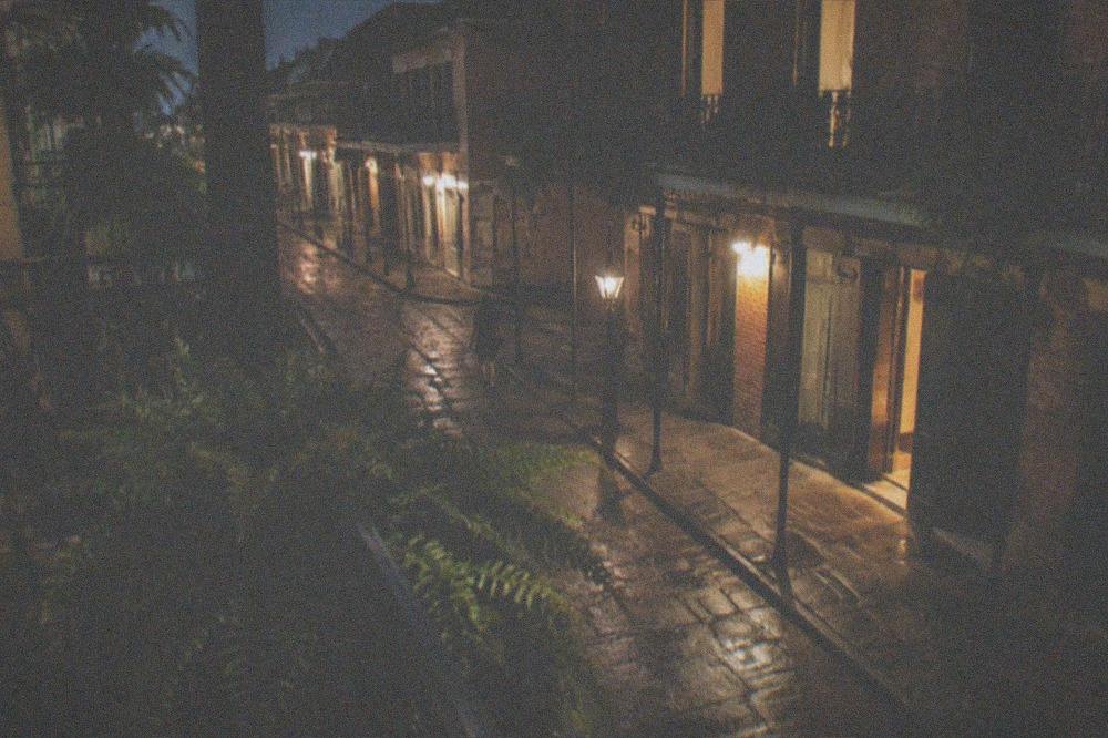 A wrought iron balcony at night overlooking an empty French Quarter street