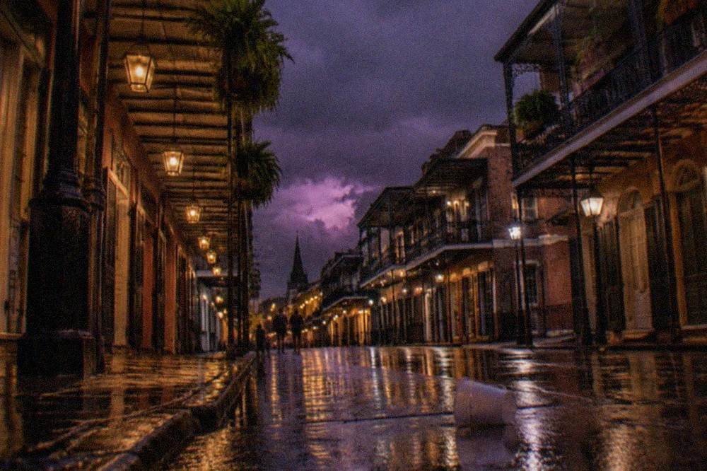 Nighttime view of a narrow French Quarter street with lit balconies and hanging lanterns