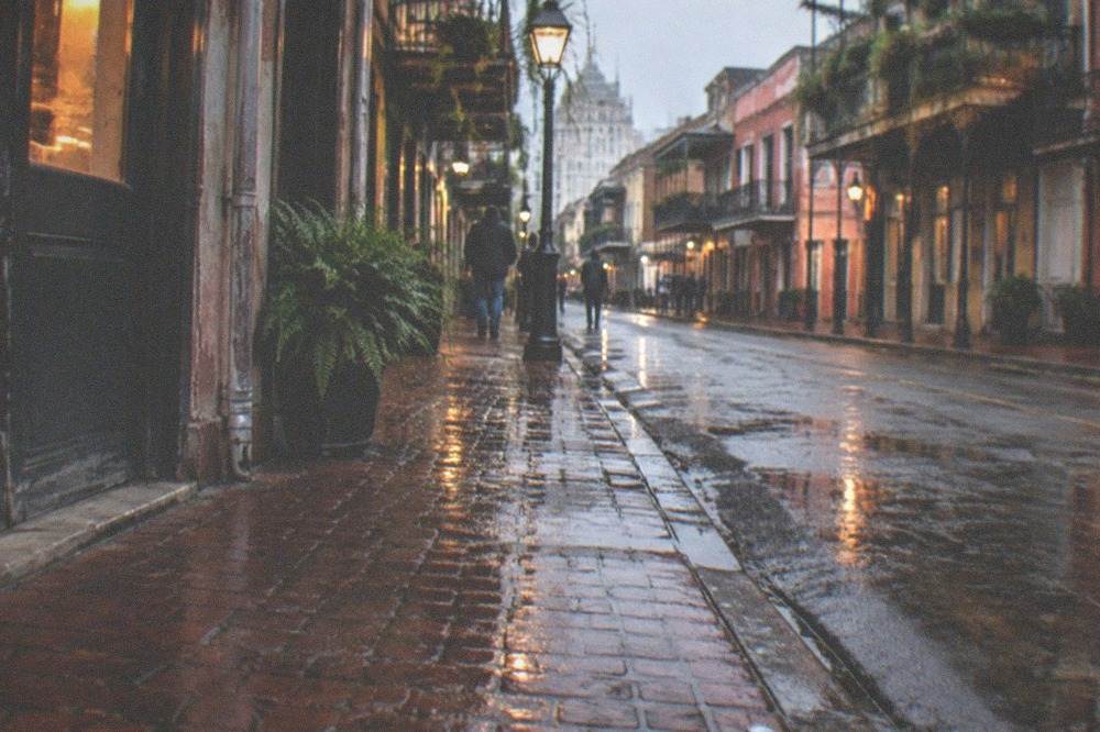 Wet brick sidewalk reflecting shop lights in the French Quarter at night