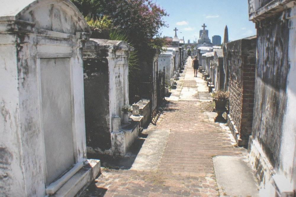 Weathered brick path between faded above-ground vaults under full sun