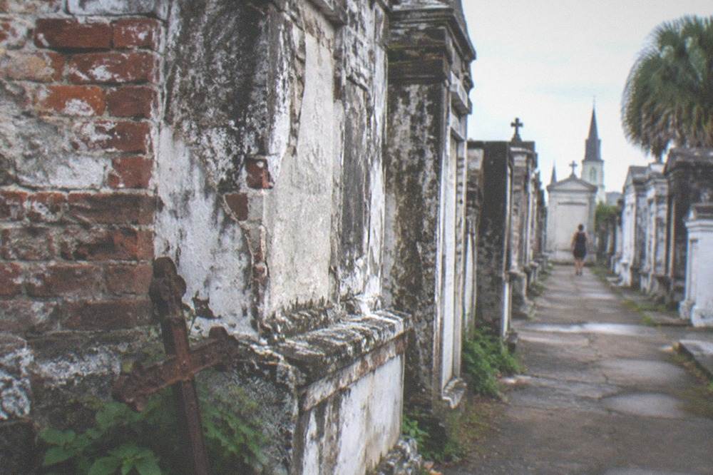 A close row of aged brick tombs with ironwork details along a cemetery walkway