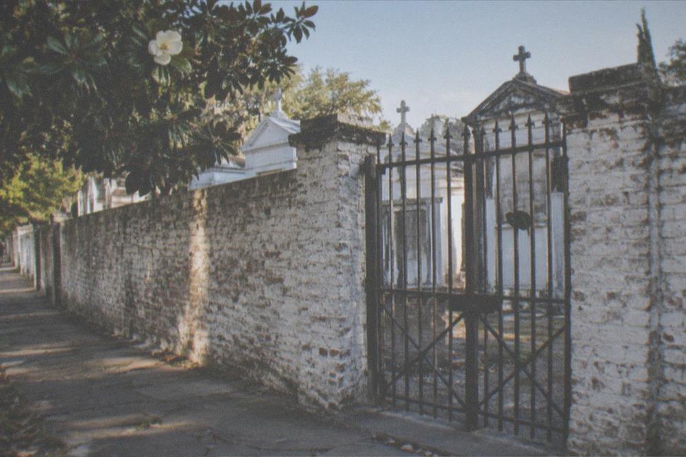 An old cemetery gate and wall at the edge of a New Orleans neighborhood under a clear sky