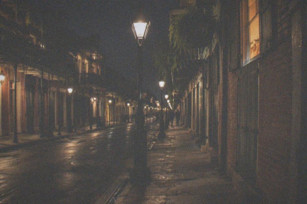 Nighttime view down a narrow French Quarter street lit by gas-style lamps