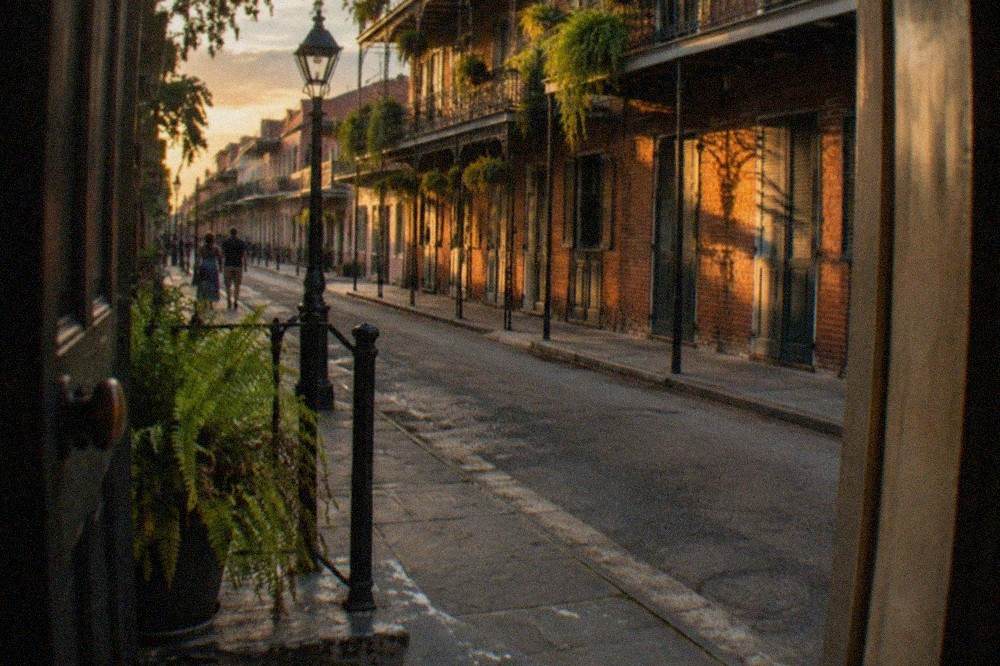 A narrow French Quarter street in warm evening light with cast iron balconies and worn brick walls