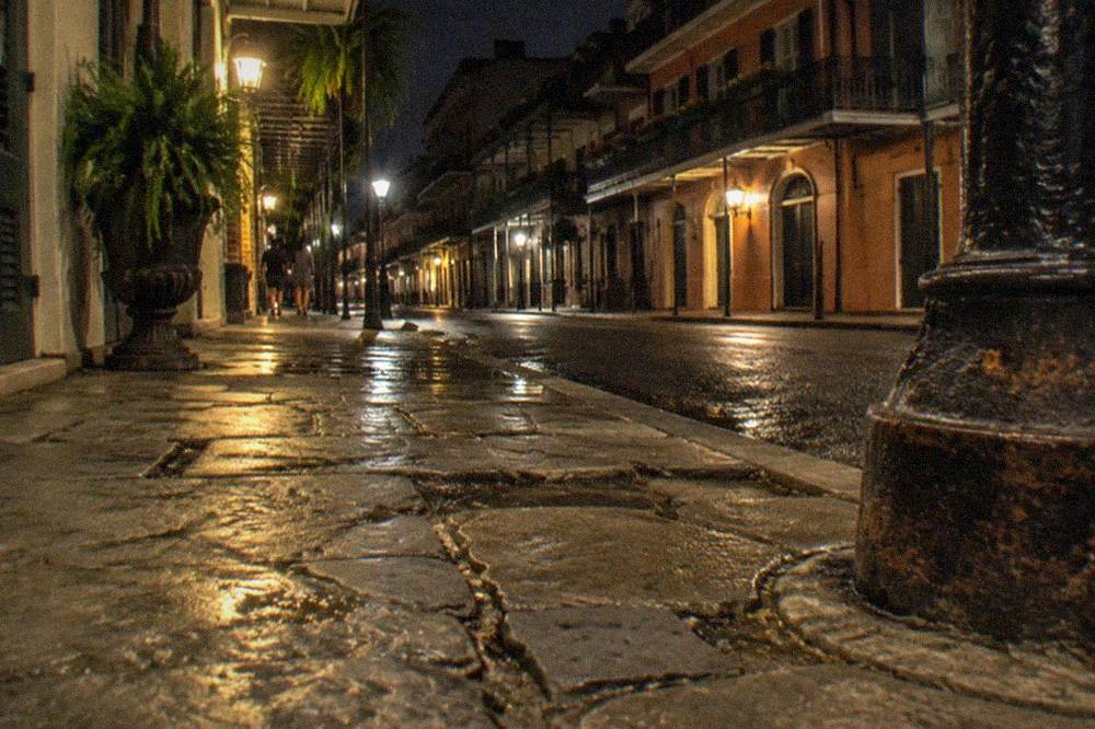 An old French Quarter sidewalk of uneven stone slabs lit by a street lamp at night